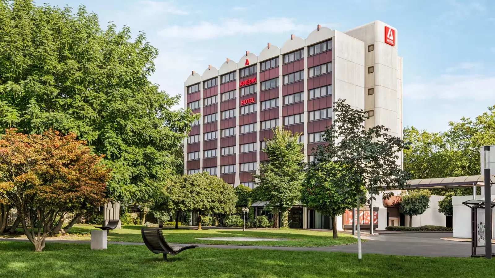 Cityhotel / Amedia Hotel Siegen with red signage and greenery in front