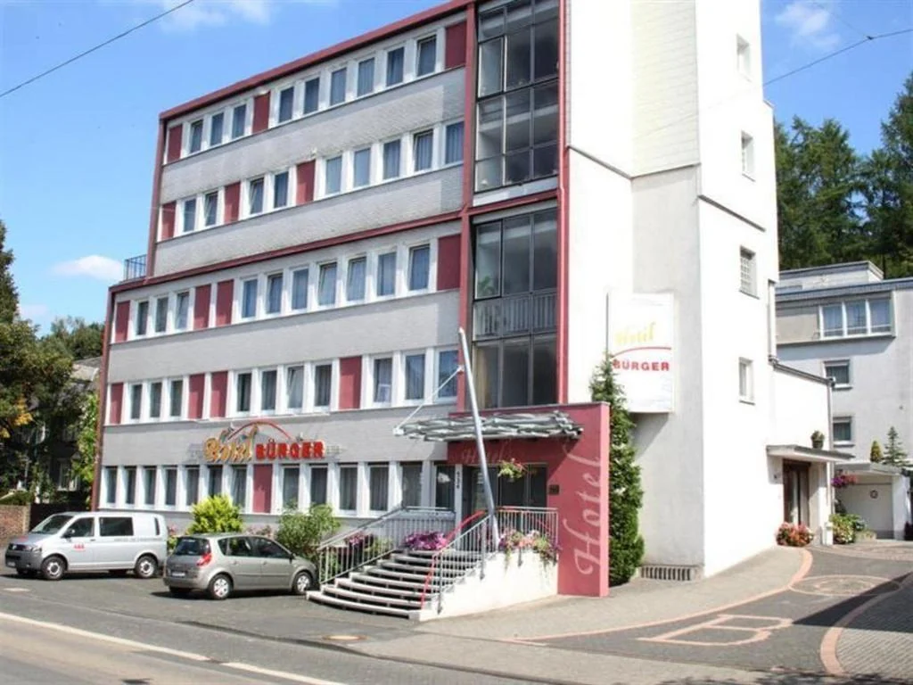 The white and red Hotel Bürger facade in Siegen, with entrance steps and parking spaces in front